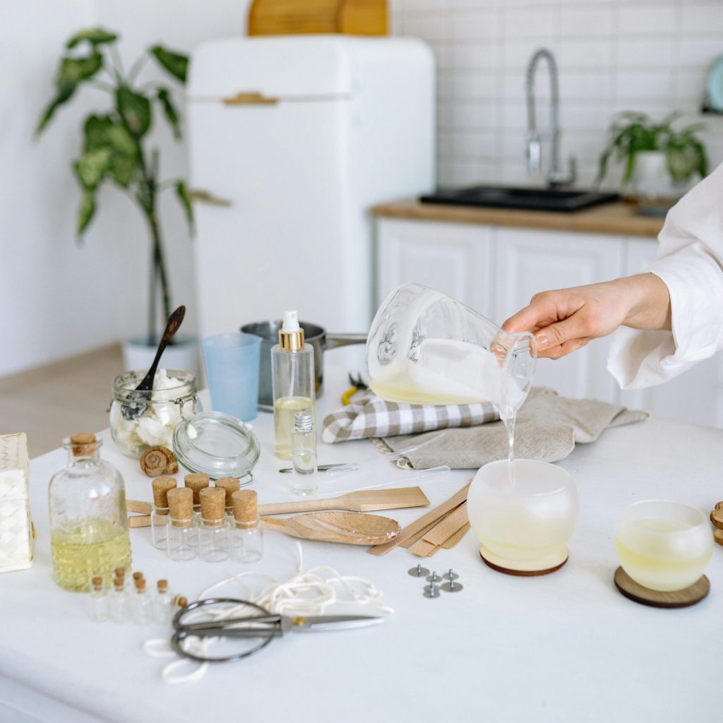Person pouring gel wax to make candles in a home kitchen setup with tools and materials.